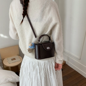 Deep brown box handbag with silver twist lock and bear charm on white knit outfit