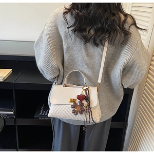 Detail of cream woven tote bag with heart charms and silk scarf on a grey sweater