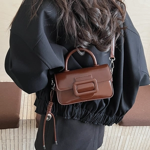 Detail view of a dark brown glossy leather crossbody bag with a large buckle and charms