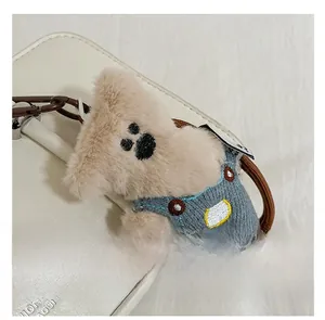 Plush teddy bear charm with blue overalls and metal clasp on white leather handbag