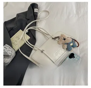 Detail of a beige PU leather crossbody bag featuring a plush bear and metal ball accents