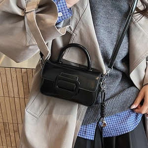 Close-up of black glossy leather square bag with large buckle on beige trench coat