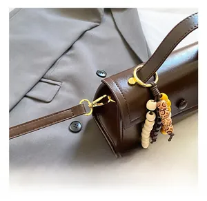 Détail du sac à main en cuir marron foncé avec crochet doré et breloque en perles de bois