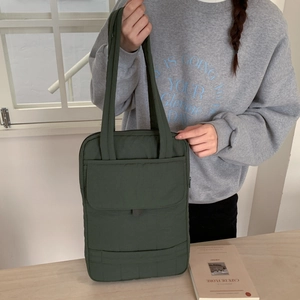 Close-up of dark green quilted tote bag with front pocket and durable nylon handles