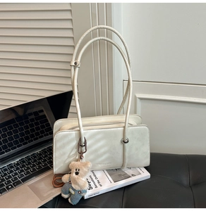Close-up of beige rectangular shoulder bag with slim handles and a cute bear pendant