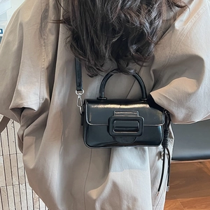Detail of a black patent leather mini square bag with a large buckle and crossbody strap