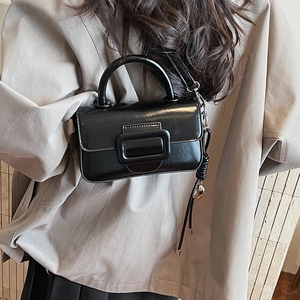 Close-up of a black glossy square crossbody bag with a tassel and metal buckle detail