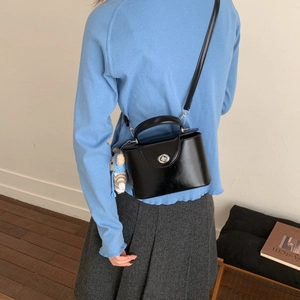 Detailed view of the black leather box bag featuring a silver metal turn-lock and knit doll