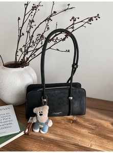 Detail view of black textured leather handbag with silver logo and cute bear charm