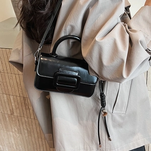 Glossy black leather crossbody bag featuring a large decorative buckle on a model
