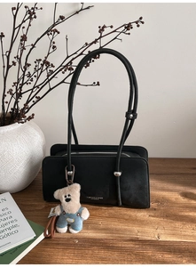 Detail of black matte shoulder bag with silver ball hardware and a plush bear charm