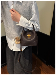 Detail of dark brown leather bucket bag with gold clasp and plush bear charm