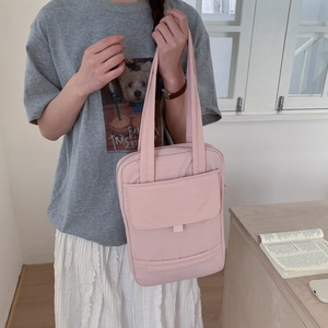 Close-up of a pale pink nylon shoulder bag with front pockets and comfortable top handles
