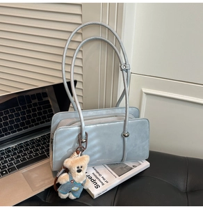 Close-up of a light blue-grey leather handbag with a plush bear charm and thin handles