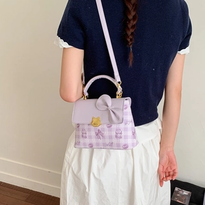 Detail of lavender square crossbody bag with bow and cat-shaped gold buckle on model
