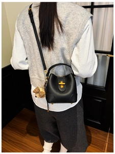 Detail of a black leather bucket bag with a plush bear charm worn by a model in a room