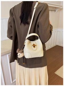 Detail view of cream bucket bag with lychee grain leather and plush puppy charm accessory