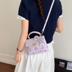 Detail of light purple bag with leather bow, gold cat clasp, and cartoon check patterns