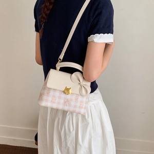 Detail of pink plaid bag with leather bow and gold cat clasp on model's shoulder