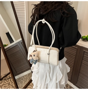 Close-up of a white glossy leather shoulder bag with a teddy bear charm in a chic setting