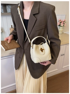 Detailed close-up of cream-colored bucket bag with lychee texture leather and gold twist lock