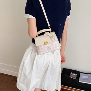 Detail of crossbody bag with cat-shaped gold buckle and bow on white-pink plaid leather