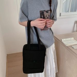 Detail view of the black minimalist crossbody bag being held by a model in casual setting