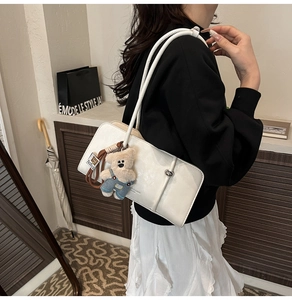 White faux leather shoulder bag with a cute teddy bear charm shown on a female model