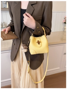 Detail of yellow bucket bag with lychee texture, metal lock, and cute bear charm pendant