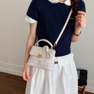 Detail of beige plaid crossbody bag with gold cat lock and decorative bow accent