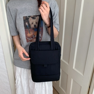 Detail of a minimalist black fabric tote bag with magnetic flap pocket and quilted design