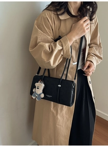 Detail view of black rectangular shoulder bag with silver studs and a cute bear charm