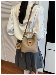 Taupe pebbled leather bucket bag with cute bear charm worn by a model in a minimalist setting
