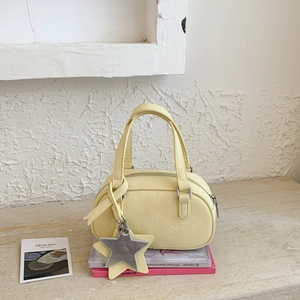 Detail of light yellow Boston bag with star charm and textured leather on pink books