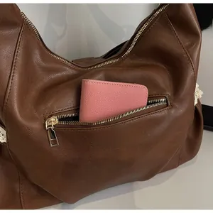 Detail view showing a large capacity zipper pocket on a brown vintage leather shoulder bag