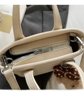 Detail of smooth silver zipper and pebbled leather texture on minimalist cream bucket bag