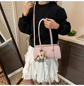 Close-up of pink rectangular shoulder bag with slim handles and a cute bear pendant