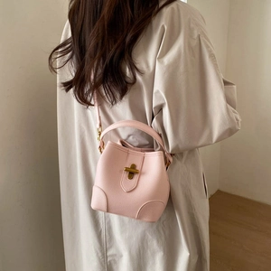 Detail of pink lychee leather bucket bag featuring gold metal clasp and crossbody strap