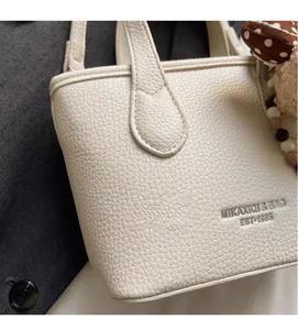 Close-up of pebble-grain cream bucket bag with MIKAXIQI logo and heart charm