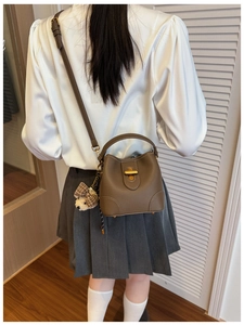 Close-up of brown pebbled leather bucket bag with golden twist lock and plush charm