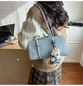 Detail of light blue leather baguette bag with silver buckle and cute bear charm