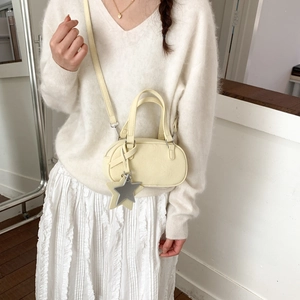 Detail of cream Boston bag with leather texture and silver star pendant on a model