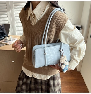 Close-up of light blue leather handbag with teddy bear charm and fashion logo detail