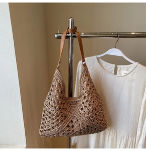 Detail of hand-woven straw tote bag with diamond cutout patterns and brown PU leather strap