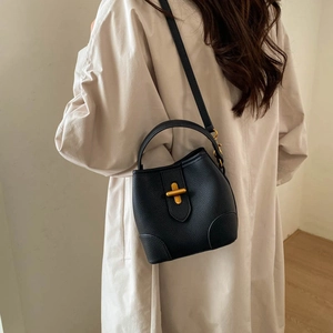 Detail of black pebbled leather bucket bag with gold cross-shaped clasp and hand strap