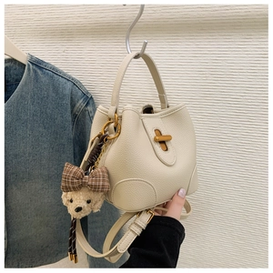 Detail of cream bucket bag with lychee texture, brass hardware, and cute bear charm
