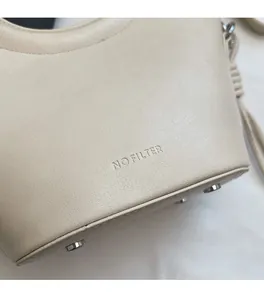 Détail d'un sac seau en cuir crème avec texte NO FILTER embossé et clous métalliques