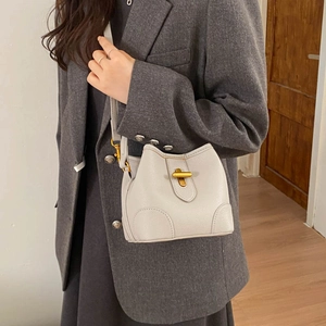 Detailed view of beige leather bucket bag with gold T-clasp and pebbled texture