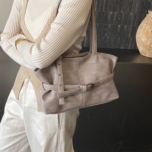 Sac à bandoulière taupe minimaliste avec détails d'œillets porté par un mannequin chic