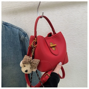 Detail of red lychee grain leather bucket bag with gold lock and teddy bear charm
